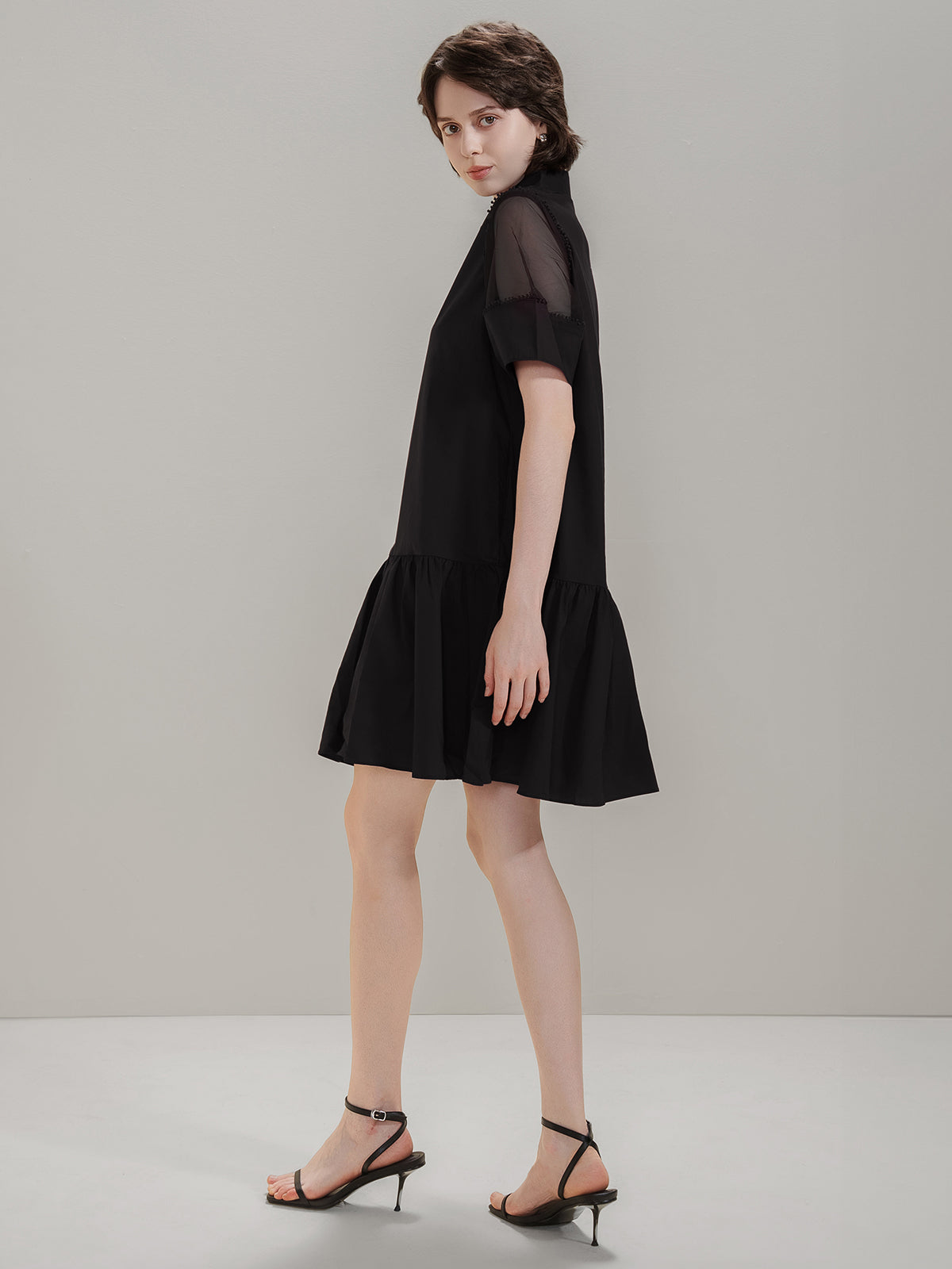 Side view of S·DEER black dress with a loose fit, mesh sleeves, and ruffled hem
