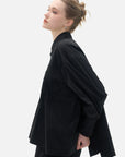 Individual black shirt with an front irregular cut and back slit, featuring a diagonal button closure.