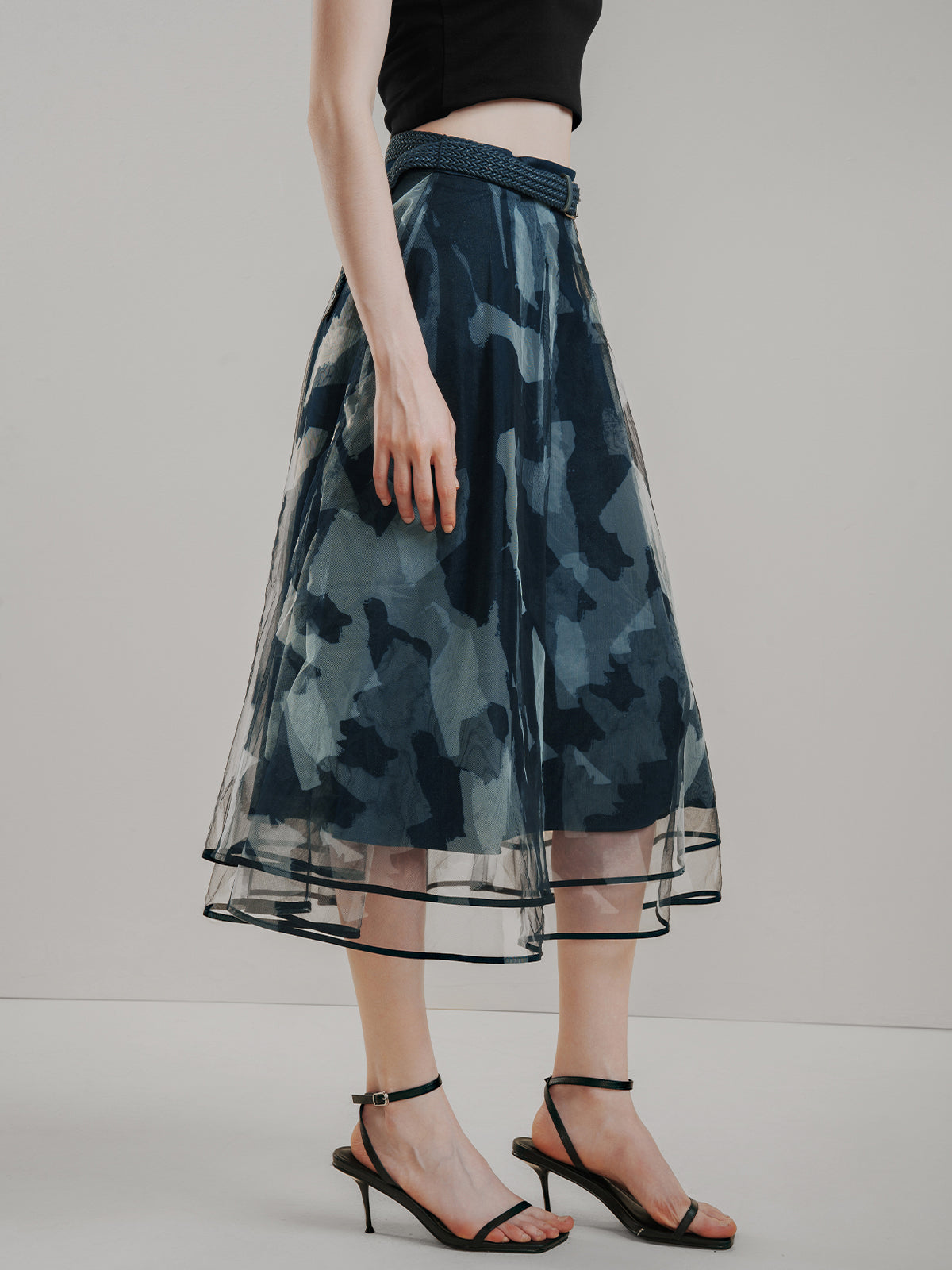 Dark blue printed midi skirt with layered tulle overlay, abstract camouflage pattern, high-waisted A-line silhouette, and matching belt, creating a stylish and edgy look for modern casual wear