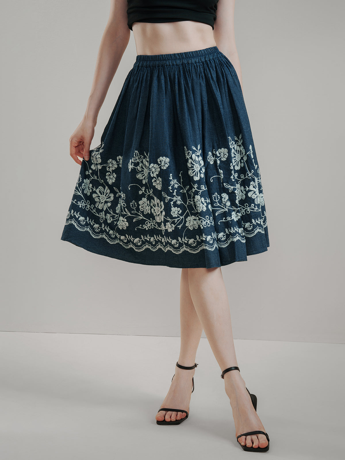 Dark blue cotton midi skirt with delicate white floral embroidery, high-waisted design, and flared A-line silhouette, offering breathable comfort and vintage charm for summer outfits