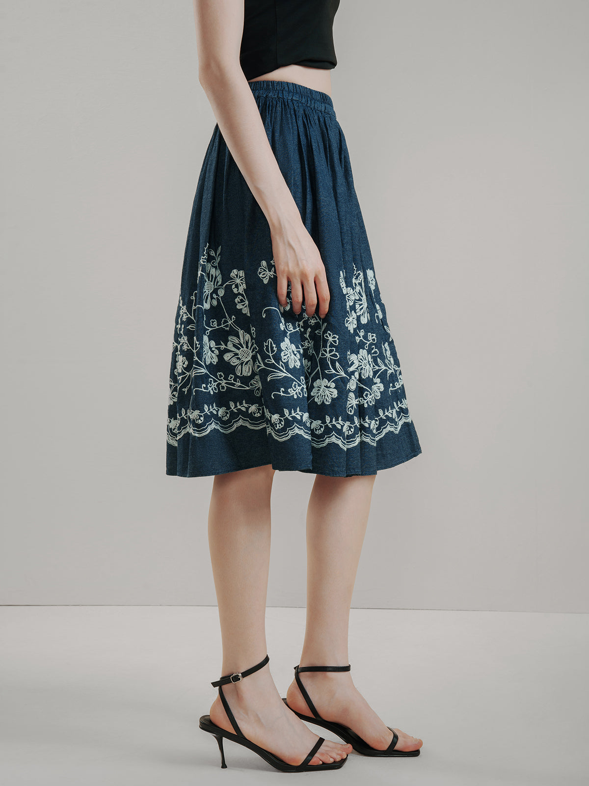 Dark blue cotton midi skirt with delicate white floral embroidery, high-waisted design, and flared A-line silhouette, offering breathable comfort and vintage charm for summer outfits